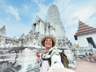 Grinning tourist in a hat in front of a white Thai stupa.vacation activities and adventure concept