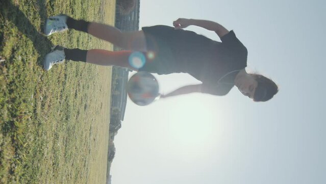 Young sportswoman juggling a soccer ball on green grass while training alone on a sunny summer day. Vertical format clip