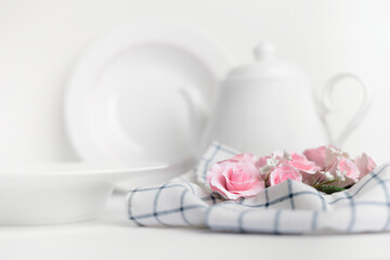 Table setting with pink roses and teapot on a white background
