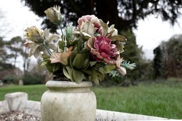 Shallow focus of fabric artificial flowers seen in a marge vase located on a large grave in a rural...