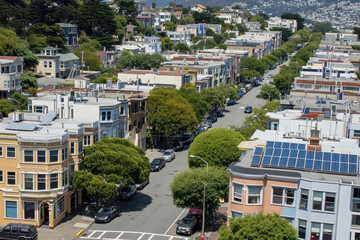 Fototapeta premium Aerial view of a sunny urban neighborhood with distinctive architecture, solar panels, and lush greenery amidst residential streets.