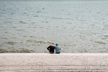 Two People Sit by a River in Lisbon Portugal