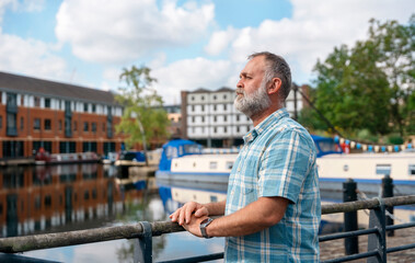 a mature bearded man sitting  on a bench, walking at a quay, enjoing warm days of the spring, summer