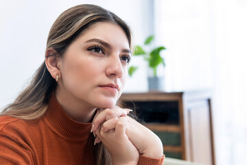 close-up of young thoughtful woman with her hands on her jaw in the living room of her home
