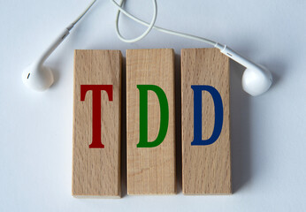 TDD - acronym on wooden blocks on white background with wired headphones