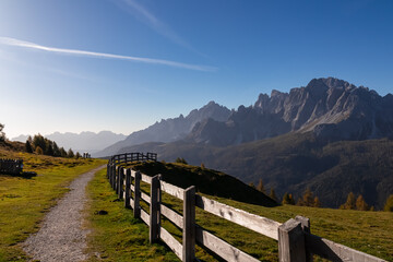 Scenic hiking trail along wooden fence on alpine meadow on Monte Gallo. View of massive mountain...