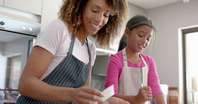 Happy biracial mother and daughter kissing while baking in kitchen, slow motion
