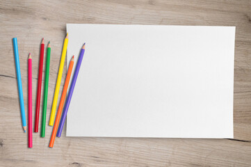 Blank paper and colorful pencils on top of the wooden table