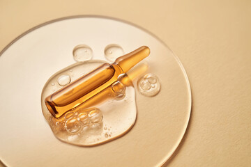 Ampoule in a drop of cosmetic gel on a beige background.
