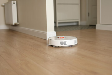 Modern wireless autonomous robotic vacuum cleaner cleans living room. Smart self-propelled white...