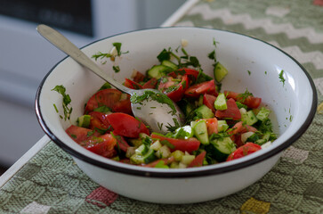 A bowl of cucumbers and tomatoes, spoon in the salad