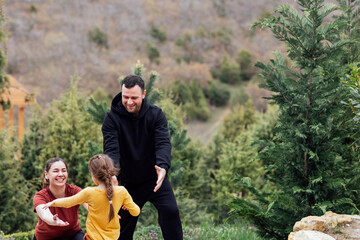 Little girl in yellow clothes runs to her joyful parents. Young smiling couple holds out their hands to their cute daughter.