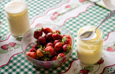 Strawberries in a bowl on the table and sour cream in jars
