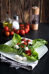 Fresh salad with cherry tomatoes, mozzarella cheese and arugula. wooden on a black background. 
