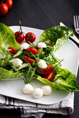 Fresh salad with cherry tomatoes, mozzarella cheese and arugula. wooden on a black background. 