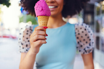 Smiling cute mixed race girl walking down the street and holding pink ice cream