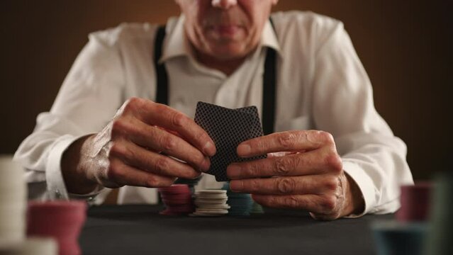 Poker game. Close up of a man's hands holding cards. He is nervous and throws the cards at the camera. An unsuccessful day for a poker player. A black table with chips on it. Brown background. RAW 8K