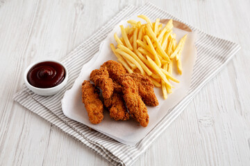 Homemade Chicken Tenders with French Fries and BBQ Sauce on a rustic wooden board, side view.