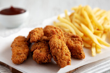 Homemade Chicken Tenders with French Fries and BBQ Sauce on a rustic wooden board, side view. Close-up.