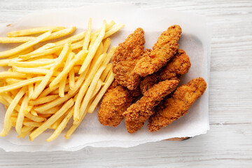 Homemade Chicken Tenders with French Fries on a rustic wooden board, top view.