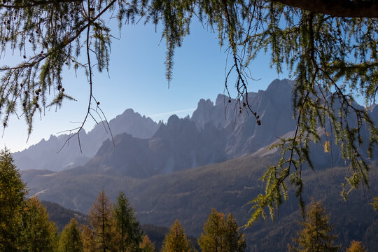 Scenic view of majestic mountain peaks Cima Bagni and Hochbrunnerschneid, Sexten Dolomites, South Tyrol, Italy, Europe. Hiking concept Italian Alps. Blue sky. Vista through golden autumn tree branches