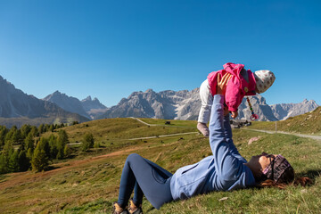 Loving mother holding baby on alpine meadow with scenic view of Sextner Rotwand, Sexten Dolomites, South Tyrol. Idyllic landscape on Klammbachalm (Malga Klammbach), Italian Alps. Tranquil atmosphere