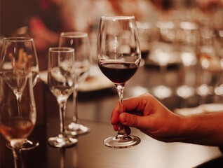 Glasses with different types of wine and human hands holding wine glasses in the background