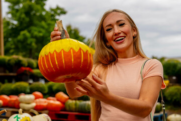 Fototapeta na wymiar A Lovely Blonde European Model Enjoys Shopping For Pumpkins And Flowers For Halloween Holiday