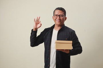 Adult Asian man smiling and giving OK finger sign while holding box package