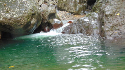 Fototapeta na wymiar Une petite cascade tombe dans un petit lac entouré de rochers