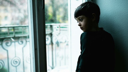 One young boy struggles with mental illness at home with green tint color. Child depressed standing by window with blank expression depicting a meaningless life