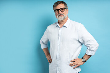 Bearded middle-aged man wearing glasses posing over blue studio background
