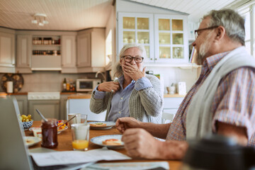 Happy senior couple eating breakfast in kitchen