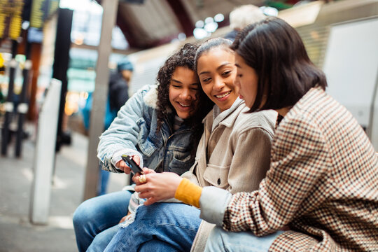 Friends looking at smartphone and laughing at train station
