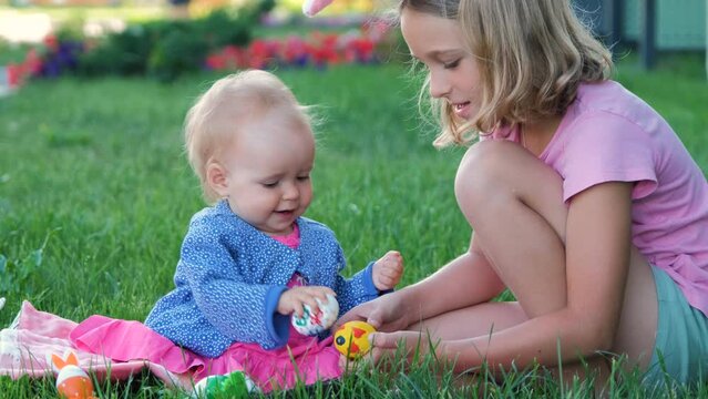Cute baby girl with her sister tapping with easter eggs while sitting on the grass after Easter hunt, slow motion
