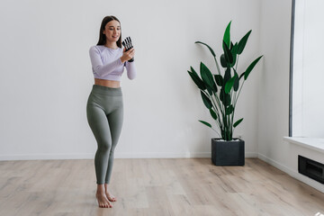 Fit woman with a bionic arm poses confidently in a home exercise space with greenery enhancing the...