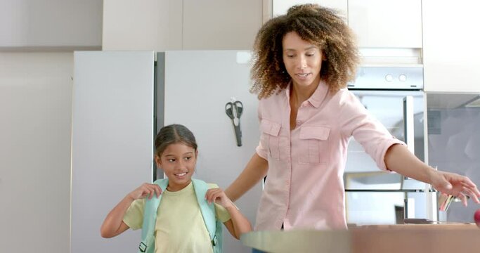 Happy biracial mother and daughter prepared for school embracing in kitchen, copy space, slow motion