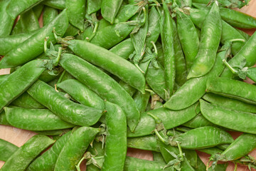 green ripe plucked pea pods on a wooden kitchen cutting board close-up. flat lay