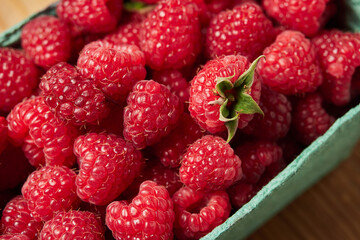 delicious fresh raw red raspberries in natural eco-friendly packaging in a green cardboard basket on a wooden table close-up. harvest. healthy food. diet. summer. vitamins