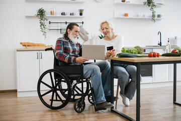 Old Caucasian couple charming wife and bearded man in wheelchair paying for food with credit card...