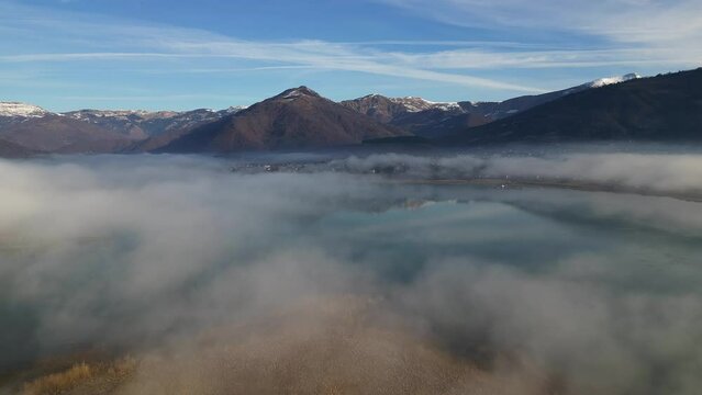 A drone flies over a mountain lake covered in thick morning fog