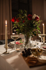 holidays, romantic date and celebration concept - close up of festive table serving for two with flowers in vase and candles burning at home on valentine's day
