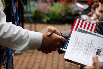 A new United States citizen receives a warm handshake and congratulations during a naturalization ceremony. - obrazy, fototapety, plakaty