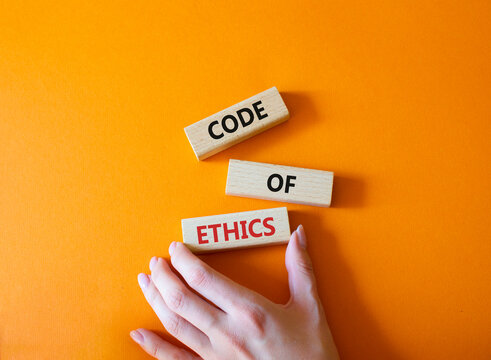Code of ethics symbol. Concept words Code of ethics on wooden blocks. Beautiful orange background. Businessman hand. Business and Code of ethics concept. Copy space.