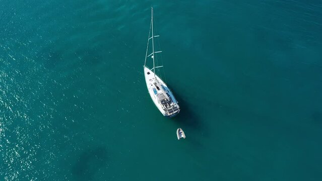 Yacht anchoring in crystal clear turquoise water in front of the tropical island, alternative lifestyle, living on a boat. Aerial view of yacht at anchor on turquoise water, showing luxury, wealth.