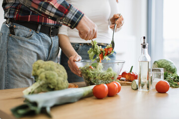 Close up of hands of senior husband and wife mixing chopped vegetables in bowl while prepare delicious healthy salad. Caucasian old couple spends free time cooking breakfast in modern light kitchen.