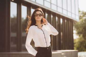 Portrait of pretty young businesswoman looking at camera while standing outdoors in city. Caucasian confident female financial consultant stands outside on stairs near office center. Business style