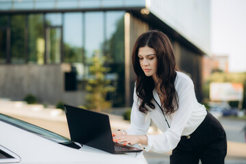 Woman entrepreneur working on laptop outside on modern building background