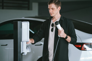 Young man travel with EV electric car to shopping center parking lot charging in downtown city...