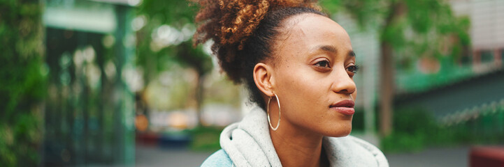 Clouse-up of nice young African American woman with ponytail in denim jacket looking around.